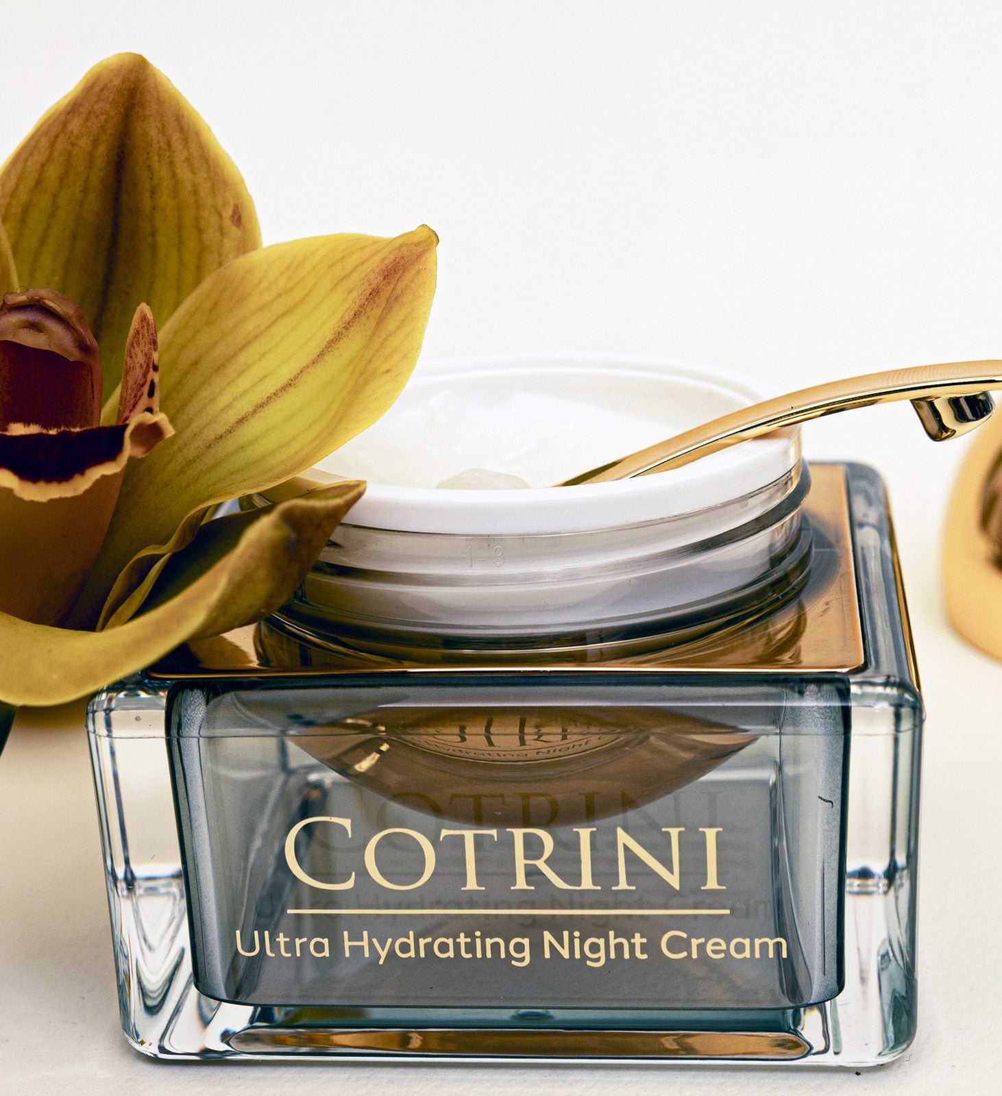 Open jar of Cotrini Ultra Hydrating Night Cream beside a yellow orchid