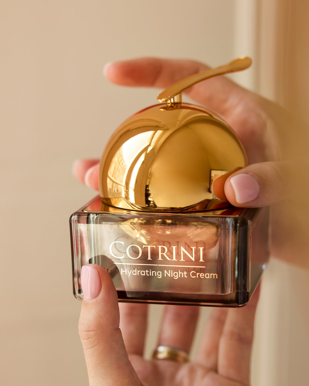 Hand holding the Cotrini Ultra Hydrating Night Cream jar with its gold dome lid